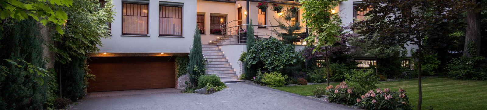 The exterior of a modern, well-maintained house, likely located in a suburban neighborhood such as Forest Hills, NY. The home features a prominent double garage with a sleek, wood-tone door set into the lower level.